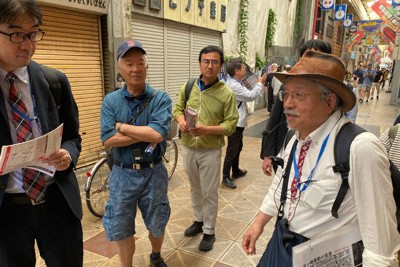 労働者支援施設や商店街を案内するありむら潜さん（右）＝大阪市西成区で、小坂剛志撮影