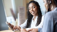 A financial planner works with her client at a table with a tablet.