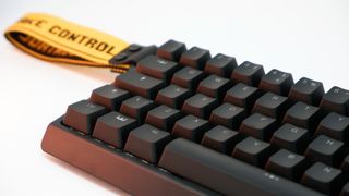 Wooting 60HE gaming keyboard pictured with yellow wrist strap attached.