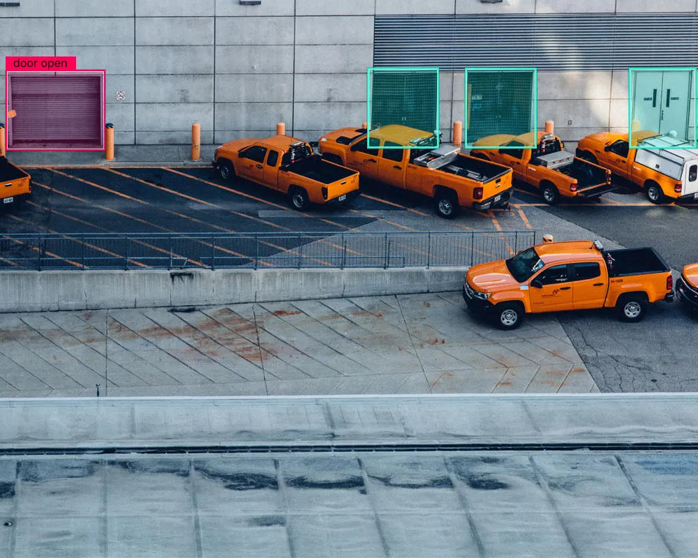 Orange pickup trucks parked along a concrete wall, with bounding boxes drawn around the closed doors, and a red box labeled "door open" around a partially open garage door. 