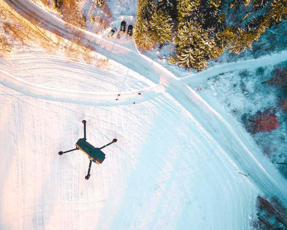 Aerial view of a black quadcopter above a snowy field.