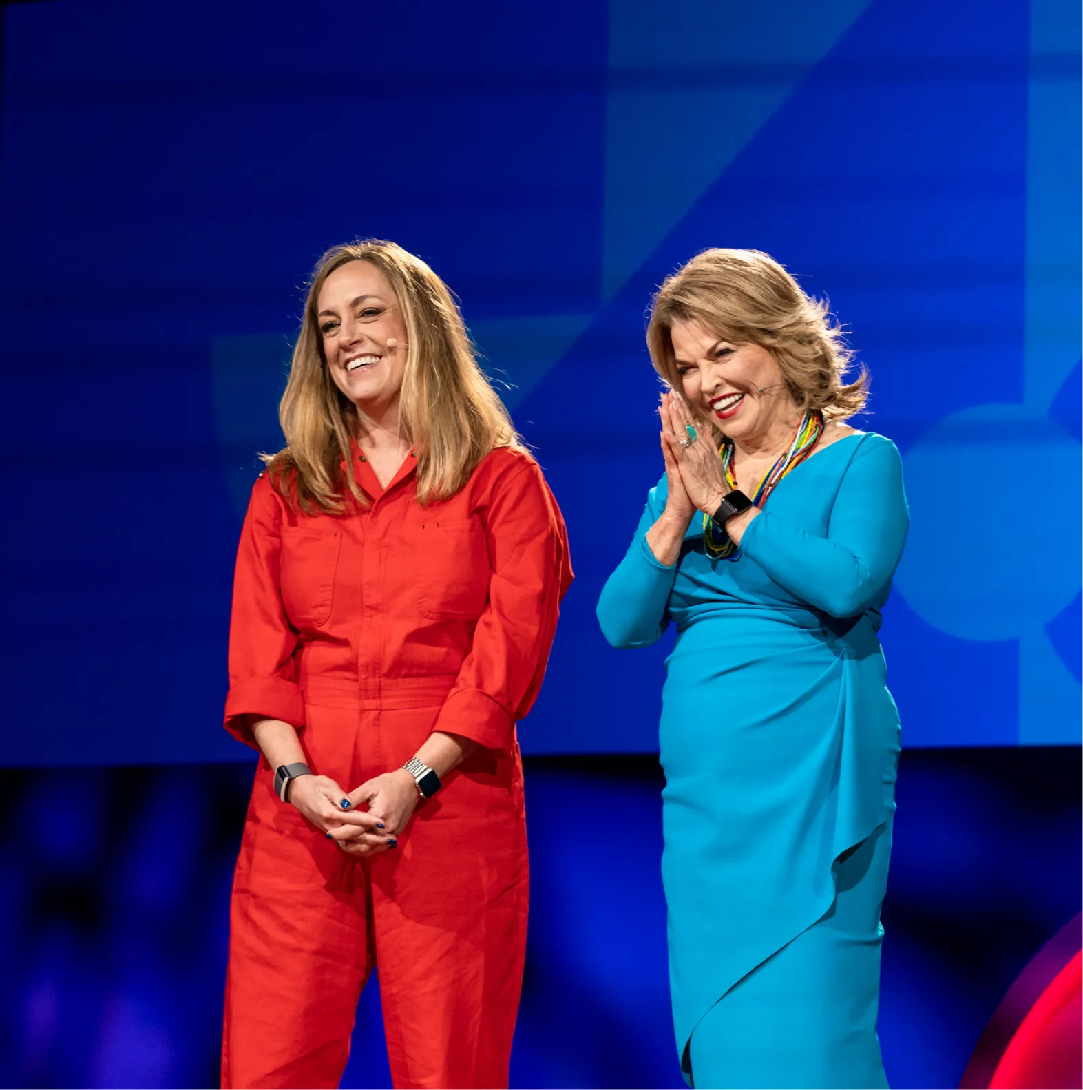 Two women speakers interact with the audience from the TED stage/