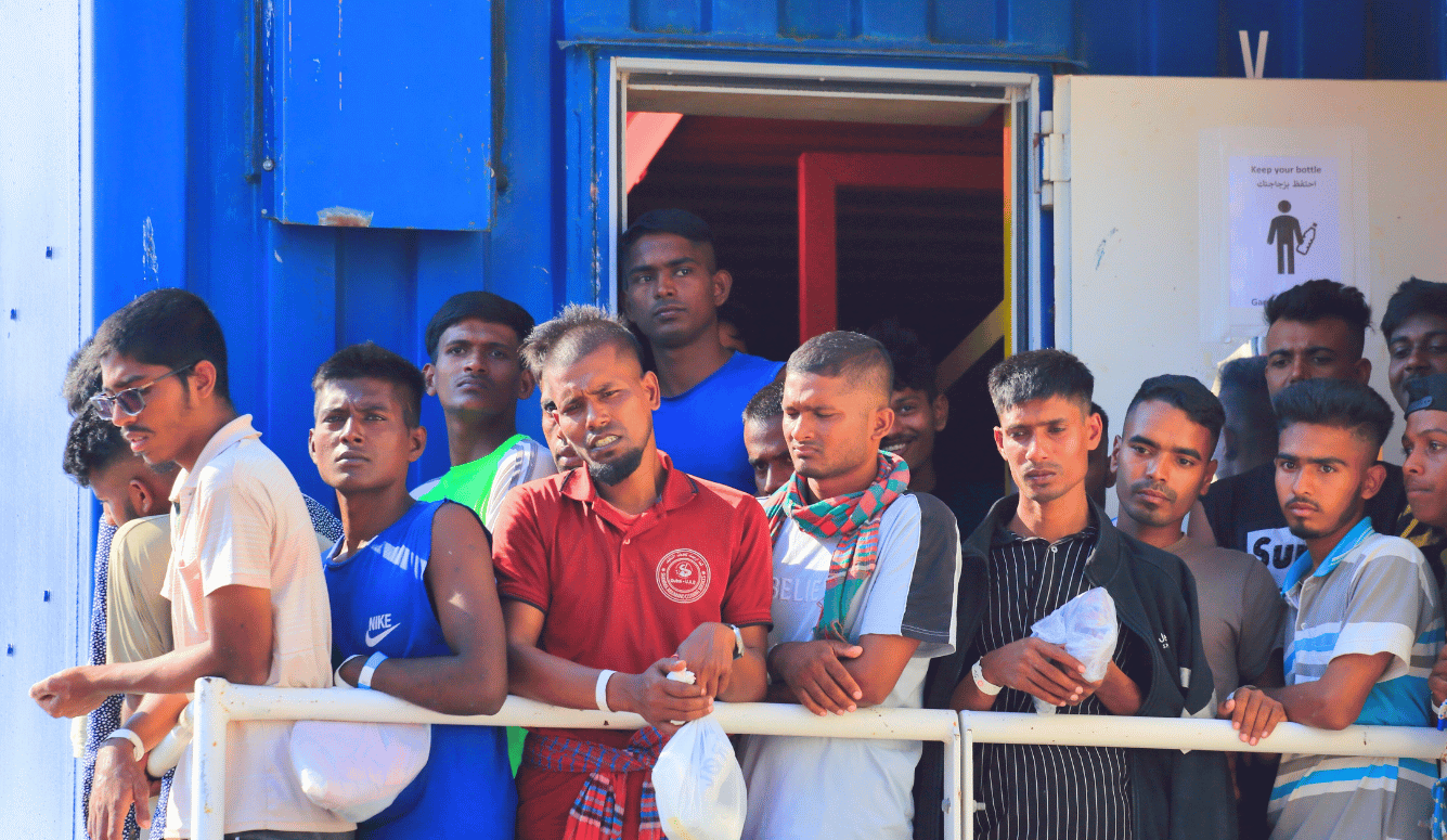 A multitude of young brown male migrants, of south-east Asian appearance, waiting on a cargo ship.