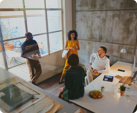 An image of four people having a meeting by a work desk. Some yellow squares outline the image at the bottom to bring a sense of energy.