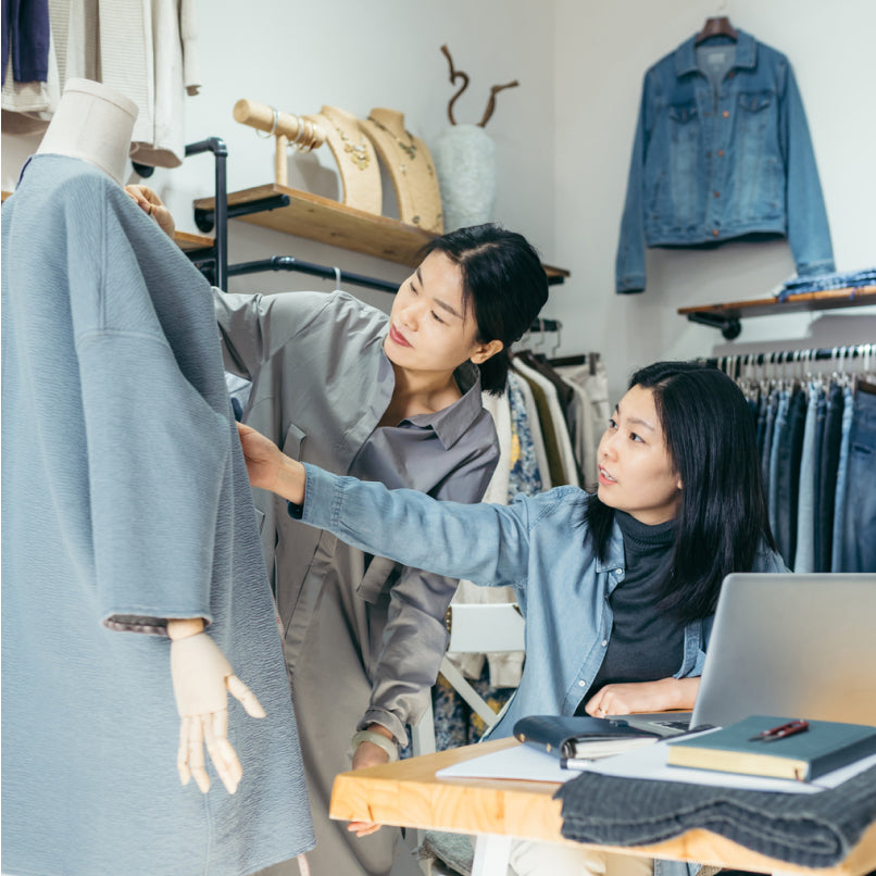 Zwei Frauen in einem Geschäft, die die Jacke einer Schaufensterpuppe anfassen. Im Hintergrund sind Jeans und Jeansjacken zu sehen.