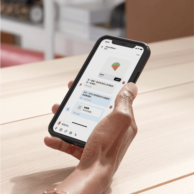 店主在後勤辦公室內用手機透過 Shopify Inbox 與顧客聊天。她在聊天時分享了一組折扣代碼，促成這筆交易。