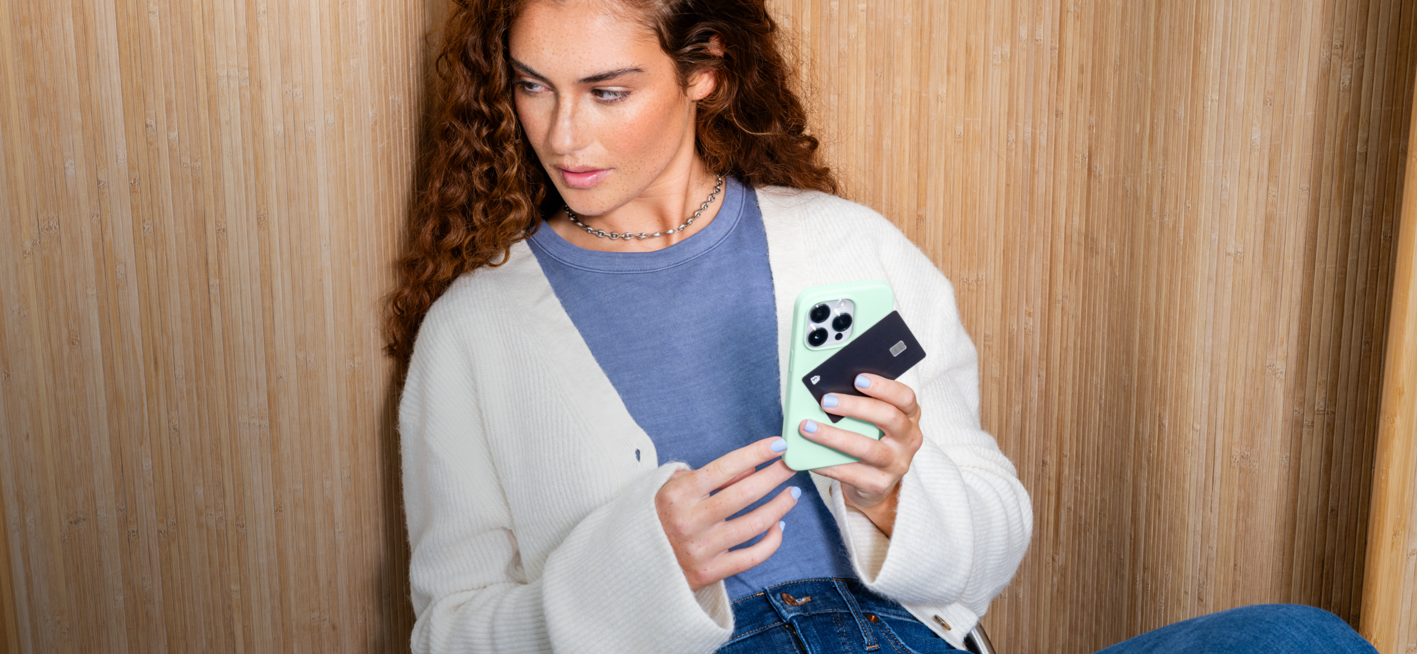 A woman with short hair wearing an orange shirt smiles while looking at her Shopify Balance account on her mobile device.