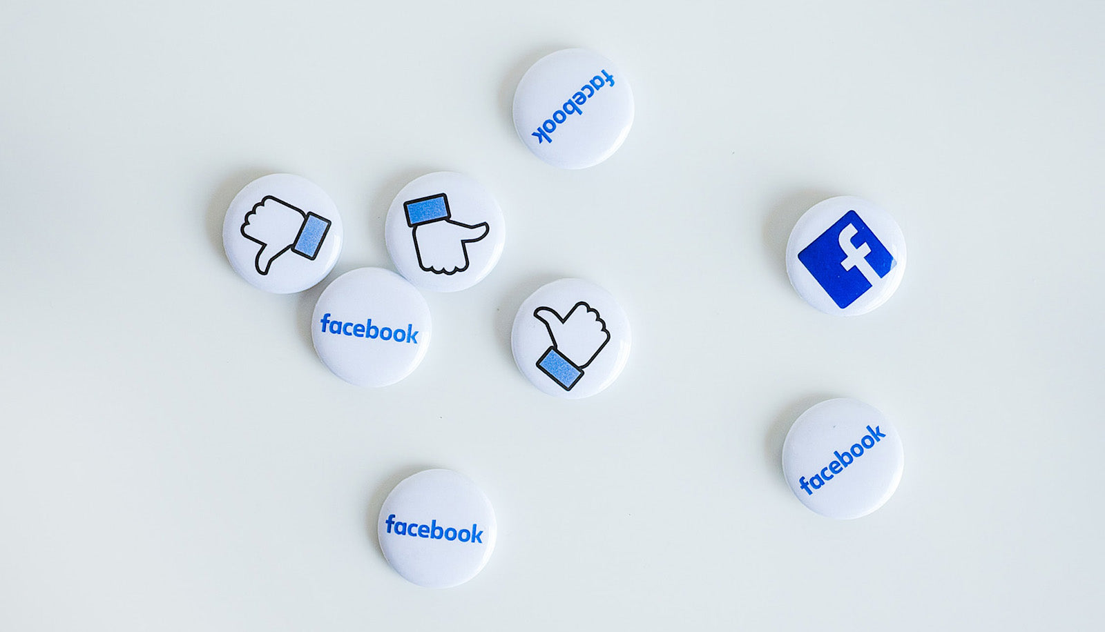 Verschiedene Buttons mit dem Facebook-Logo, -Schriftzug und Gefällt-mir-Icon liegen auf einem weißen Tisch