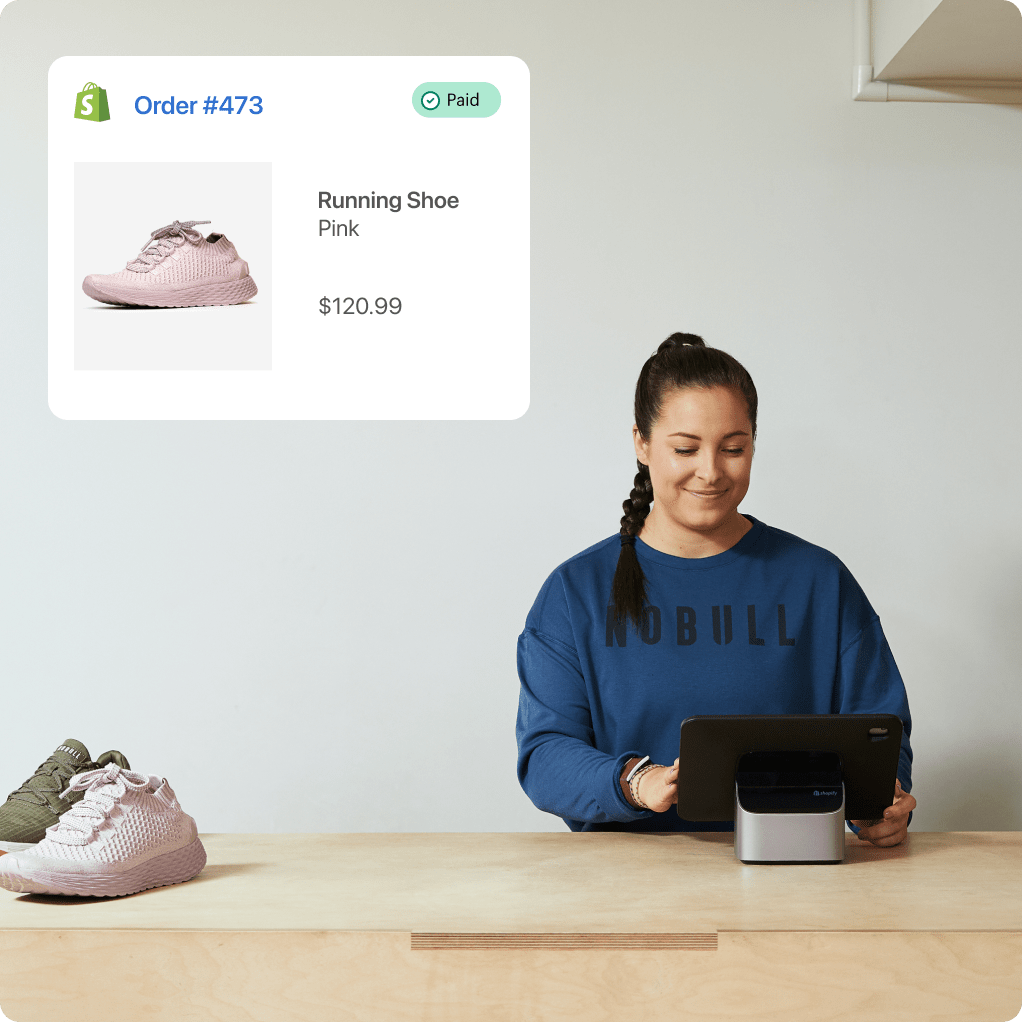 A smiling woman sits at a counter, smiling at a tablet device in front of her. There are two shoes to the left of her, and in the upper left, an order paid confirmation screen with a shoe, a description of “Running shoe - pink” and a cost of $180.42.