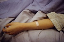 A patient's arm lies flopped on a bed, a bandage on the forearm