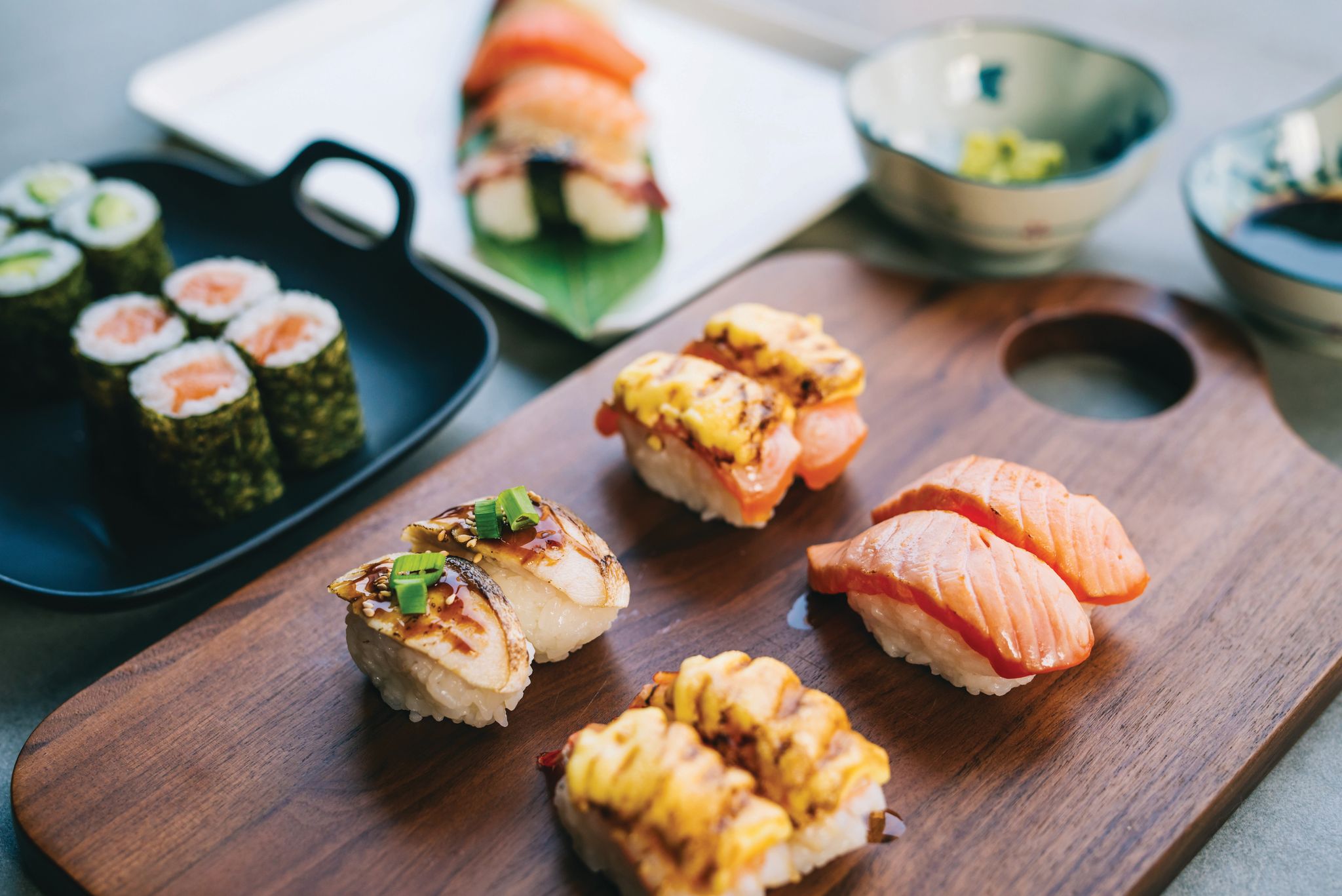 Four pairs of nigiri with a roll and other sushi in the background.