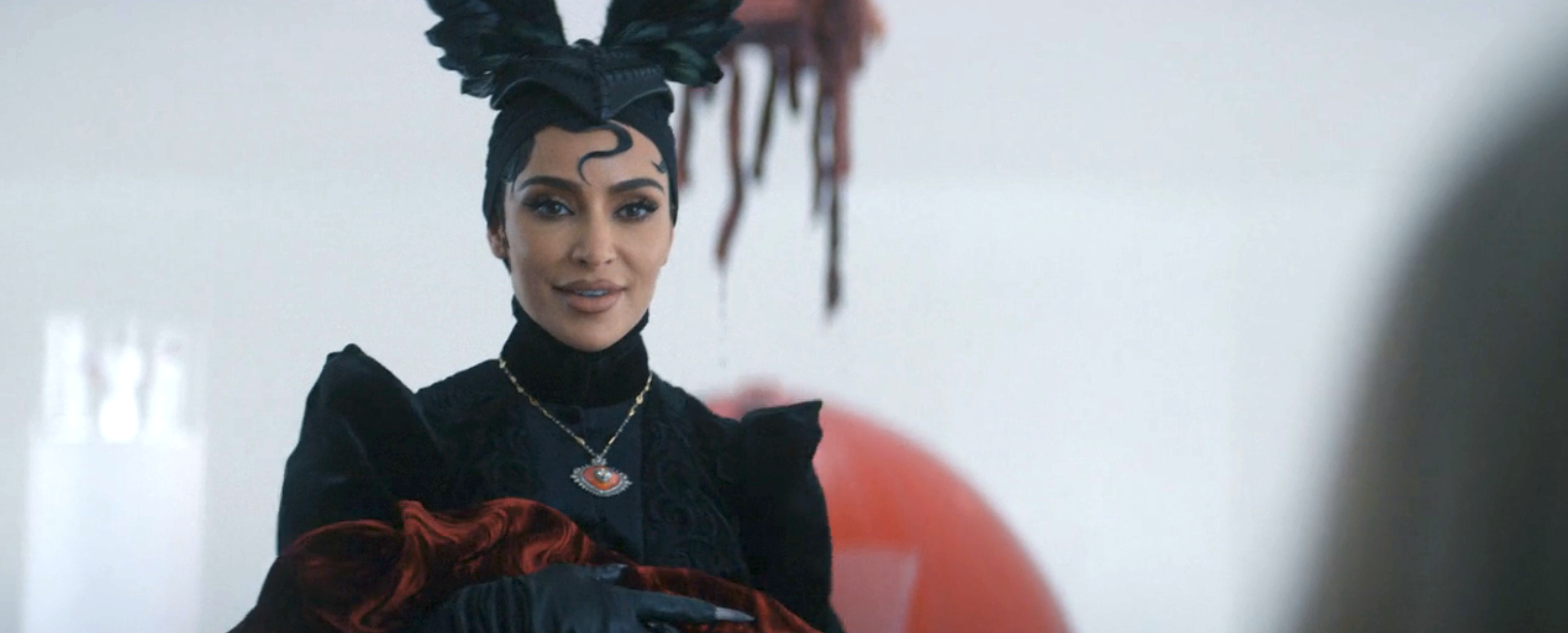 Kim Kardashian in a black feathered headdress, holding a baby, in American Horror Story: Delicate