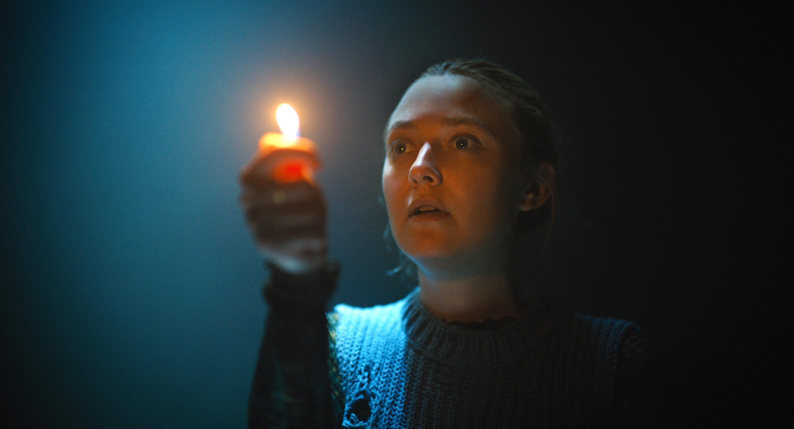 Mina (Dakota Fanning) holds up a lighter with the flame lighting her face as she explores a dark cavern in Ishana Night Shyamalan’s The Watchers