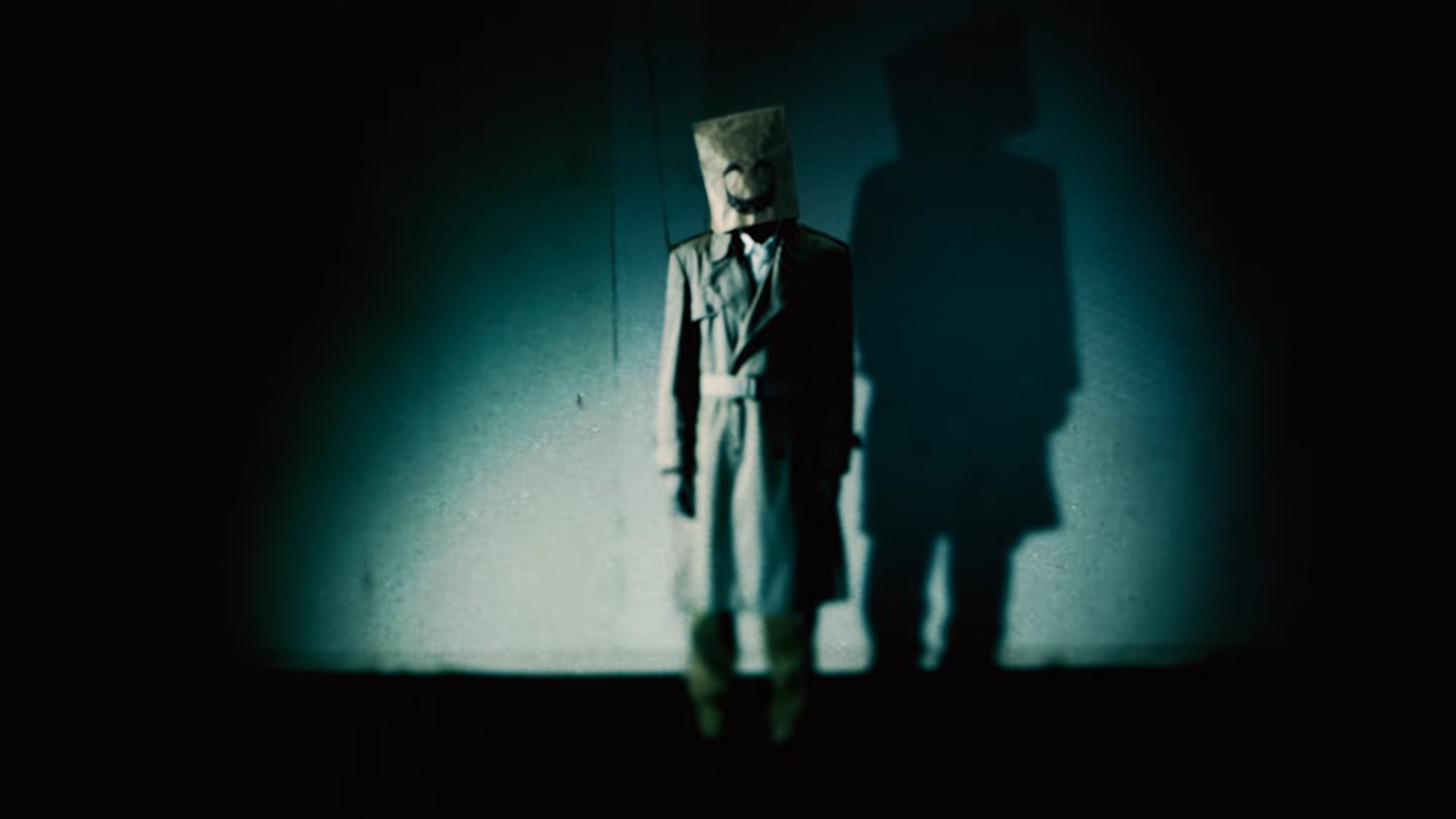 An image of a man wearing raincoat and a paper bag with a smiley face drawn on it over his head from Nintendo’s teaser for Emio