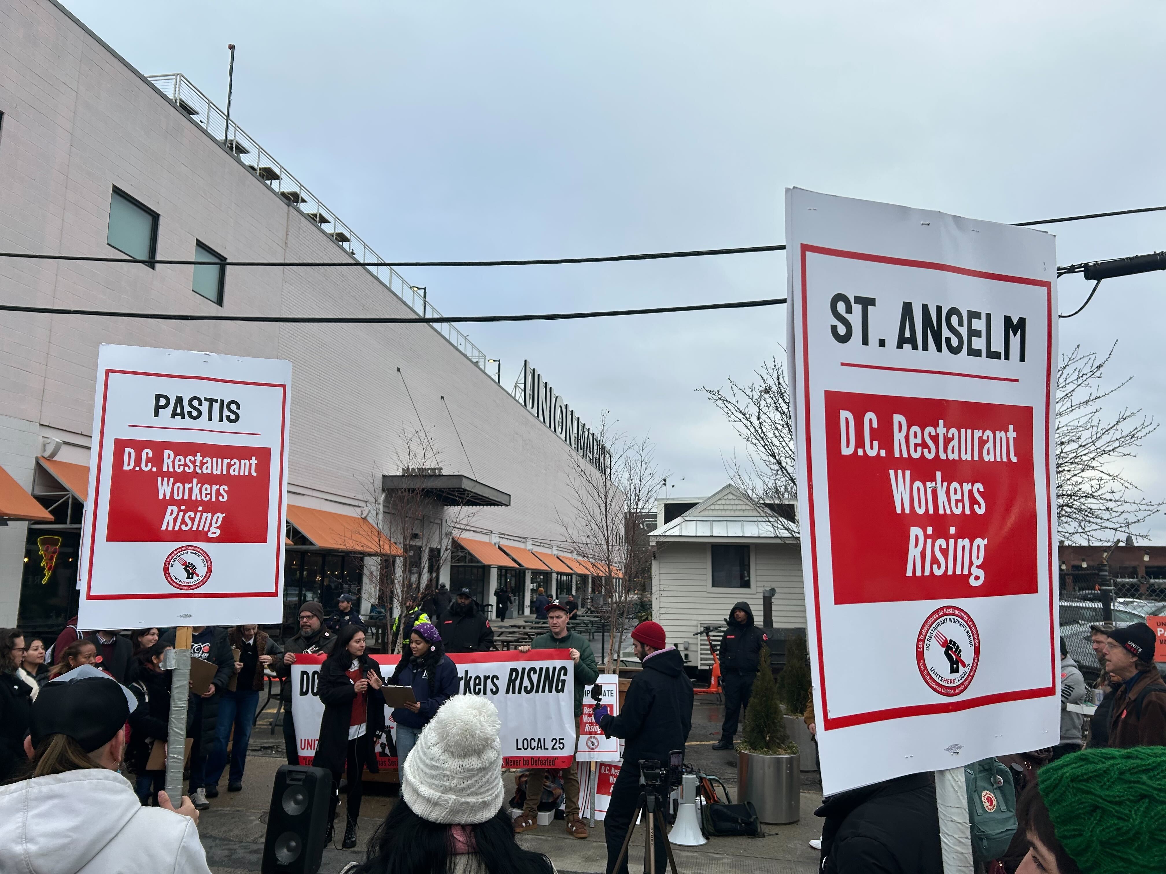 People stand outside protesting with red and white signs.