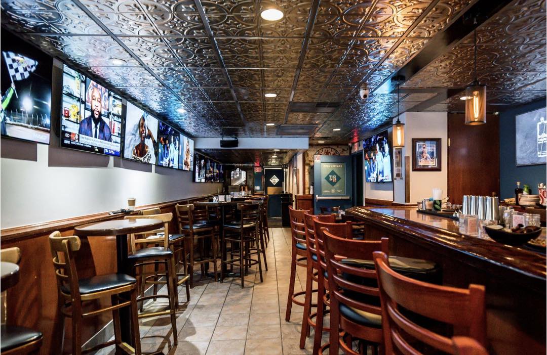 A bar with a metal ceiling, wooden chairs, and TVs 