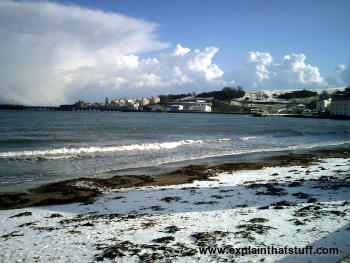 A snowy beach in winter looking at the sea and the clouds. Illustrates the three states of water: solid snow, liquid sea, aerosol water vapor cloud.