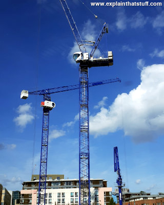 Three white tower cranes against a cloudy blue sky in Bristol, England.