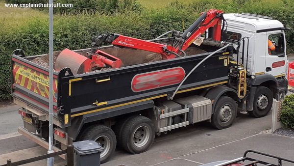 A hydraulic crane mounted on the back of a road construction truck.