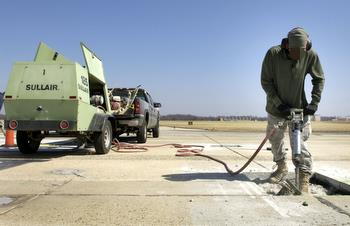 Jackhammer being used on road, linked to compressor by air hose