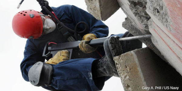 Naval rescue worker attacks a concrete structure with a jackhammer pneumatic drill.