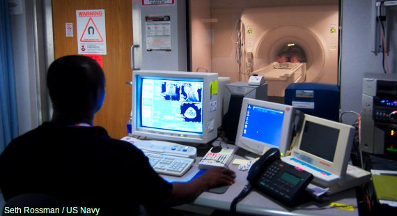 A patient undergoes an fMRI scan while a technician watches the scan forming on a computer monitor.