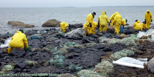 Photo of yellow suited workers cleaning up shoreline after oil pollution spill.