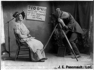 An old-fashioned photography session with a tripod camera and the photographer crouching under a cloth.