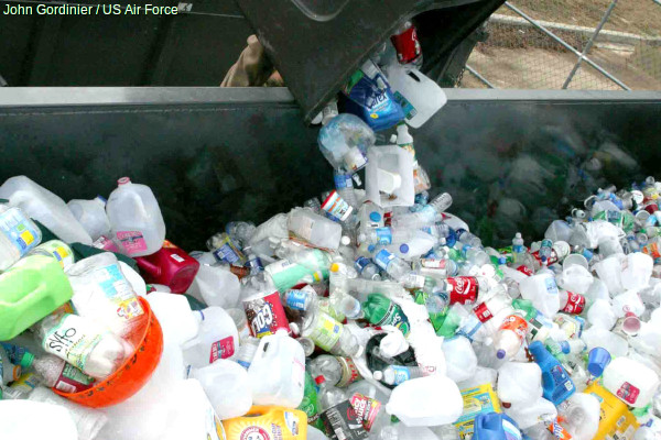 Plastic bottles being tipped into a recycling dumpster