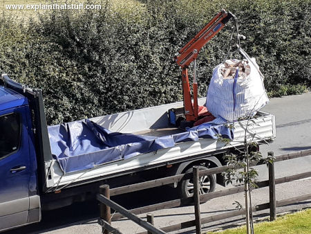 A hydraulic crane mounted on the back of a small blue Mercedes truck.