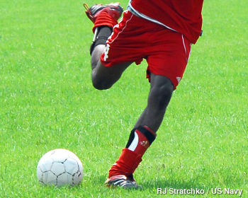 A soccer player kicks a ball over green grass.