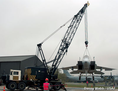 A truck crane with a lattice book lifts an airplane