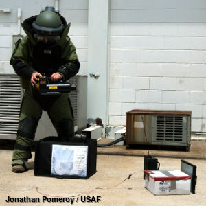 A security person wearing protective body armor uses X rays to check the contents of a suspicious package.