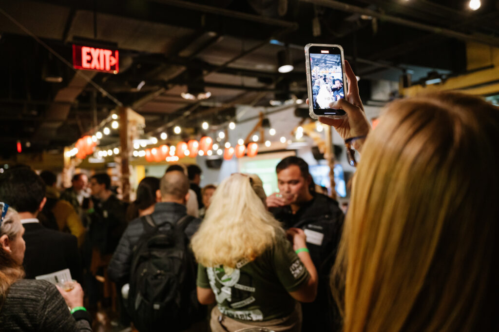 People socializing at a CIC event while a woman takes a photograph with an iPhone