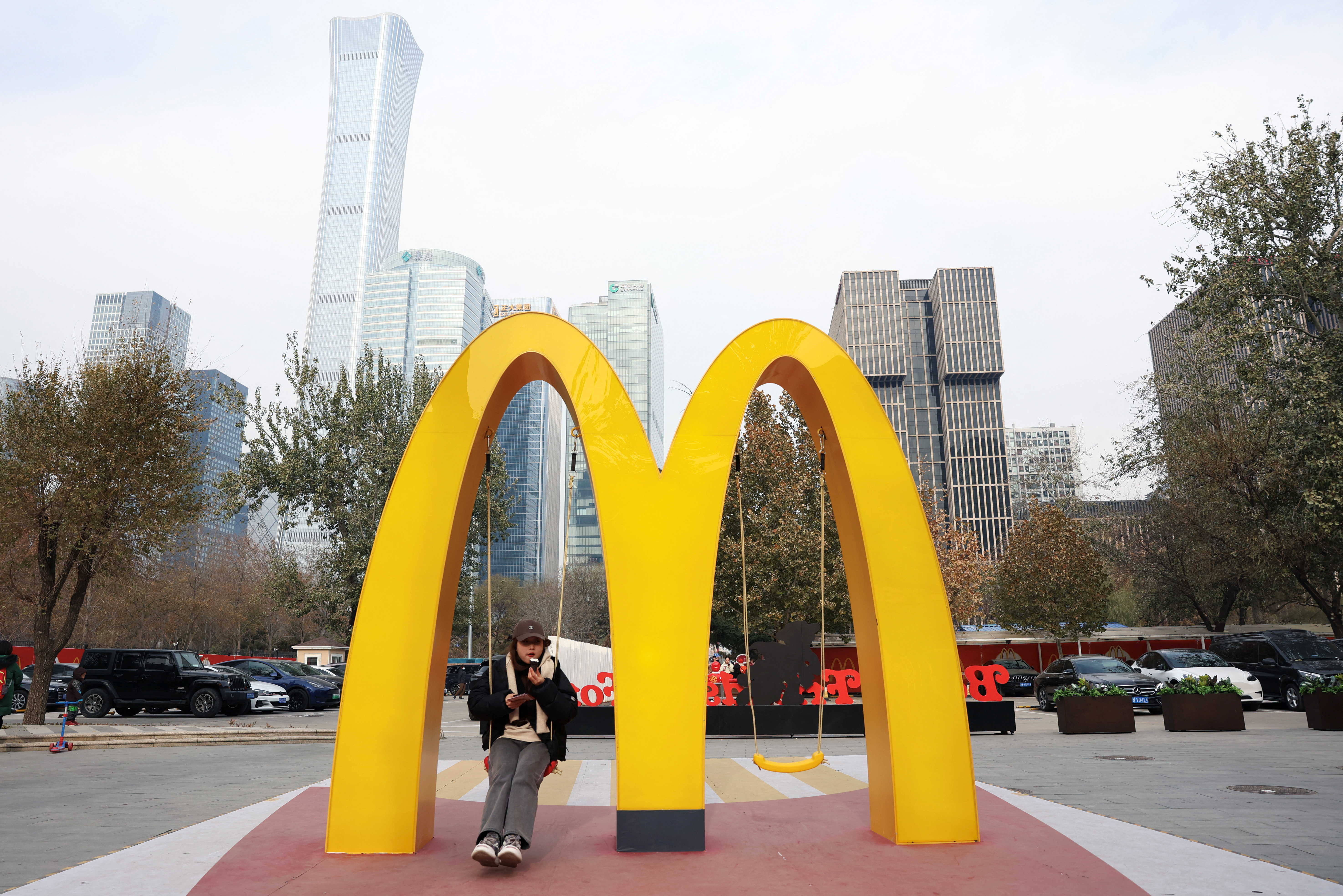 A woman sits on a swing attached to a giant sign of McDonald's, outside its themed exhibition in Beijing