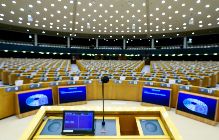 A lectern is shown against a backdrop of empty desks set up for a parliamentary meeting.