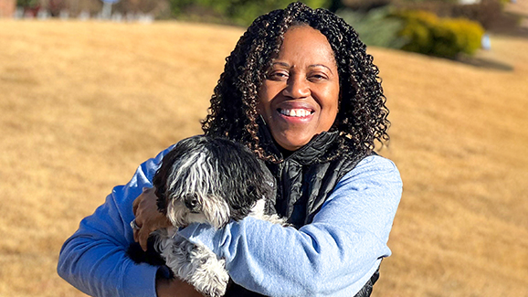 Ayopo Jones, a Finance Director with AWS, holds her dog and smiles in an outdoor setting.