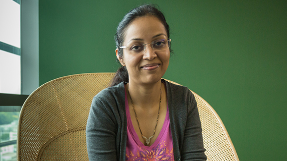 Arthi Jaganathan, Solutions Architect with AWS, smiles at the camera with a green background.