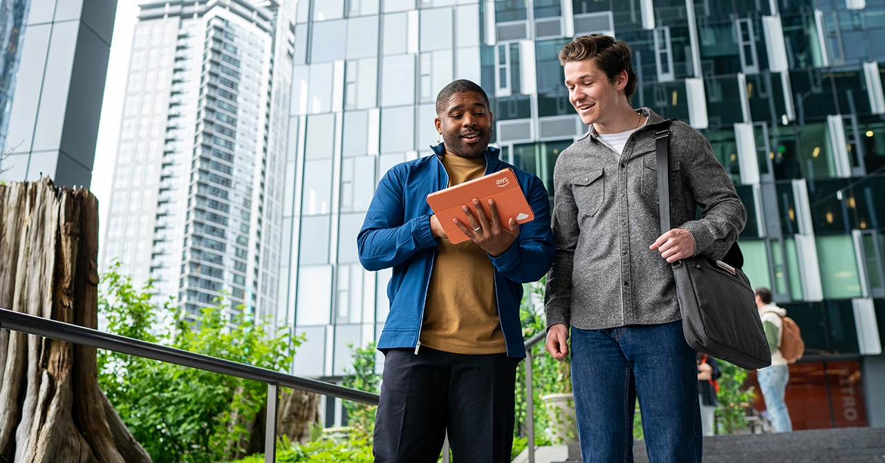 Two AWS employees stand outside an office looking at a tablet together.