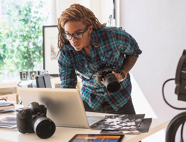 Man holding a camera, looking at pictures on a laptop