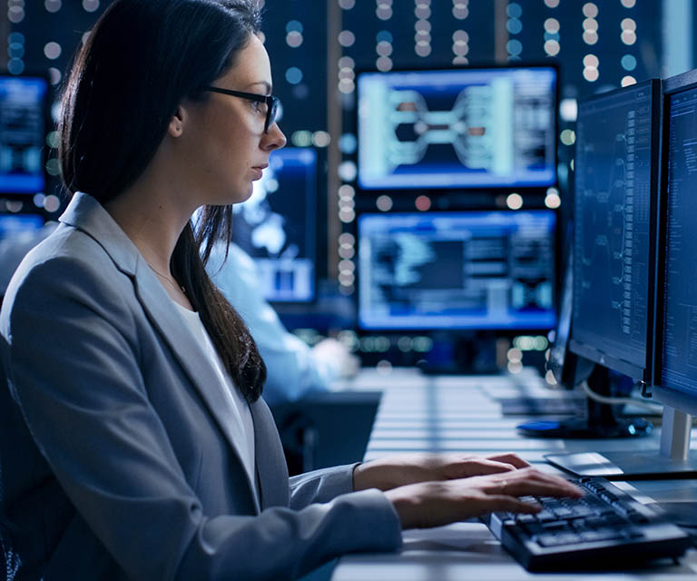 Female Engineer Controller Observes Working of the System. In the Background People Working and Monitors Show Various Information. 