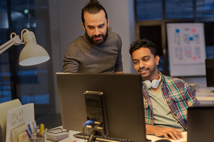 Two male colleagues reviewing data on desktop computer while working late in office