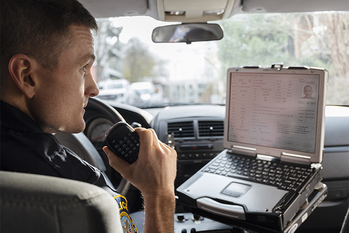 Police officer talking on radio while using a laptop in patrol vehicle