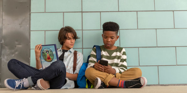 Two boys sitting at school and looking at a phone.