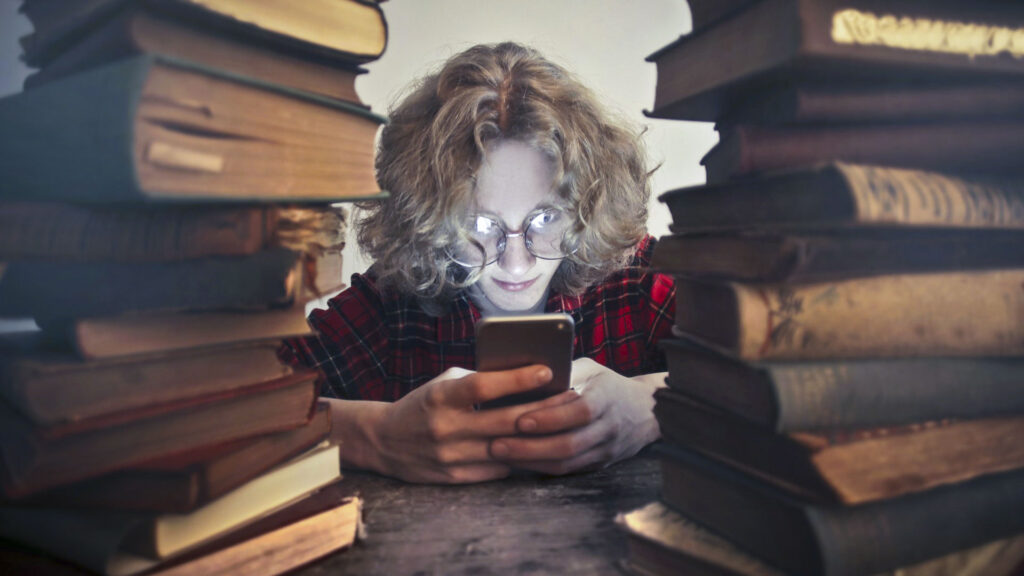 person using phone between piles of used books