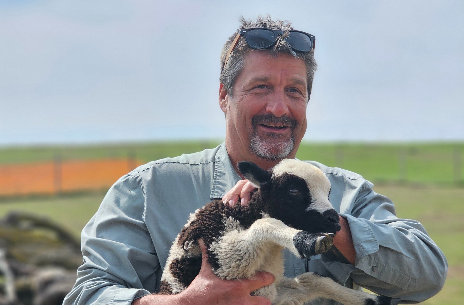 Jim holds a baby calf while standing outside. 