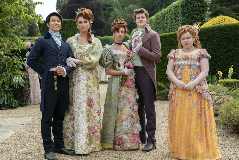 Bessie Carter as Prudence Featherington, Harriet Cains as Philipa Featherington, Lorn Macdonald as Albion Finch, Nicola Coughlan as Penelope Featherington stand together outdoors in season 3 of 'Bridgerton'