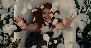 Emily Carey as Harriet Manners lays in a tub with rose petals falling around her during a photoshoot in Season 1 of 'Geek Girl'