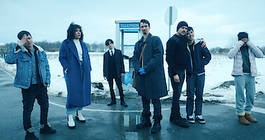 Umbrella Academy cast in an outdoor scene, standing in front of a telephone booth. 