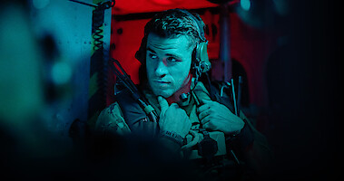 Liam Hemsworth as Sgt. JJ Kinney wears a military uniform while riding in a helicopter in ‘Land of Bad’